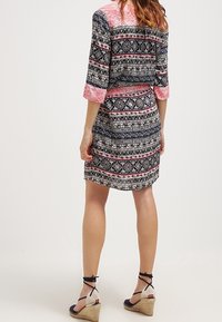 Robe courte arborant un motif géométrique multicolore avec du noir, du rose et du blanc. Elle possède des manches trois-quarts et une taille cintrée.