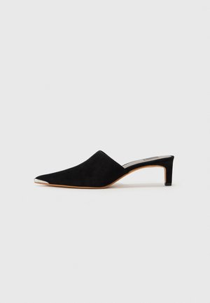 Mule in suede nero con punta scoperta e punta a forma appuntita, con un accento metallico argento sulla punta, caratterizzata da un tacco basso e sottile.