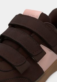 Baskets en velcro marron avec un matériau en daim, une rayure d'accent rose et une semelle texturée marron. Marque visible sur la languette.