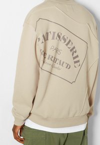 Beige sweatshirt met een grafische print met de tekst "Patisserie Paris" op de achterkant. Heeft een ontspannen pasvorm en geribbelde manchetten. Geweldig voor casual dragen.