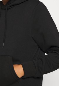 Sudadera negra de material suave, con un bolsillo tipo canguro y puños acanalados. Incluye un cordón en la capucha y un diseño sin adornos.