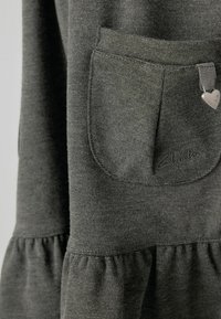 Szara sukienka z tkaniny o teksturowanej powierzchni, zebranym dołem, przednią kieszenią oraz małą metką w kształcie serca.