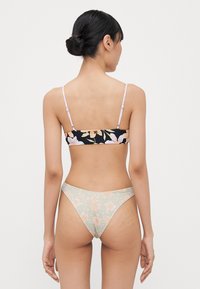 Bikiniset med en svart blomstret bralette og lysegrønn blomstret bikiniunderdel. Justerbare stropper, glatt tekstur, minimal dekning.