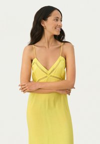 Gelbes ärmelloses Kleid mit tiefem V-Ausschnitt und Spitzenverzierungen. Leichter Stoff mit fließender Form, der bis zur Mitte der Wade reicht. Einfaches Design.