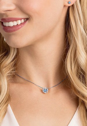 Sterling zilveren ketting met een ronde, lichtblauwe edelsteen hanger omringd door kleinere heldere stenen; bijpassende stud oorbellen zichtbaar.