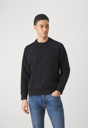 Sort sweatshirt med præget logo foran, rund halsudskæring og ribbede cuffs. Bæres med blå denim jeans. Klassisk pasform og minimalistisk design.