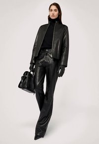Schwarze Lederjacke mit Reißverschluss, kombiniert mit hochtaillierter schwarzer Lederhose. Accessoires umfassen schwarze Handschuhe und eine strukturierte Handtasche.