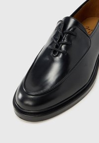 Sort lædersko med en glat overflade, rundet tå og snørebånd. Har diskrete syninger og en lav gummisål.