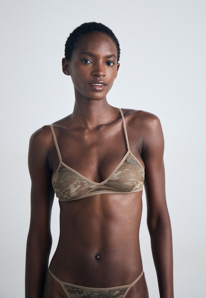 Camo-patterned bikini set in tan tones. Lightweight, textured fabric with thin straps and minimal coverage. Logo accent on the bra.