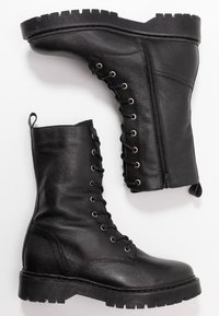 Svarta läderkängor i militärstil med en texturerad yta, snörning framtill, sidodragkedja och en kraftig gummisula med ett räfflat mönster.