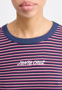 T-shirt a righe nei colori blu navy, rosso e bianco con collo rotondo. Presenta il testo "Santa Cruz" ricamato in bianco sull'area del petto.