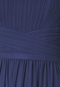 Temno modra obleka z naborki na zgornjem delu, širokim gladkim pasom v pasu in tekočo krilo spodaj.