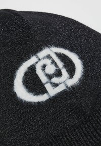 Berretto lavorato a maglia nero con un logo bianco peloso. Il materiale ha una leggera lucentezza, con una vestibilità aderente e senza decorazioni.