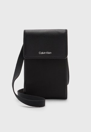 Zwarte Calvin Klein crossbody tas met klep en verstelbare stoffen riem, gemaakt van gestructureerde en gladde materialen.
