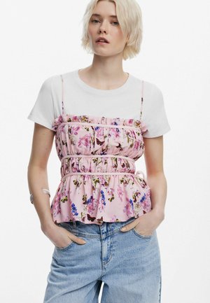 Top de peplum floral en rosa, con un diseño con volantes y tirantes ajustables. Combinado con una camiseta blanca y jeans de mezclilla.