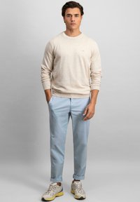 Pulover tricotat bej, chino light blue și adidași bej. Ținuta are un design casual cu o croială lejeră și mansete răsucite.