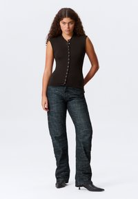 Mørkebrun, ermeløs topp med høy hals og knapper foran. Kombinert med litt utvidede, strukturerte mørke denimjeans og spisse svarte hæler.