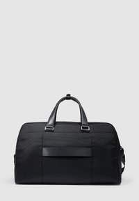 Bolsa de lona negra hecha de tela texturizada con asas de cuero, que cuenta con un bolsillo frontal y detalles de herrajes plateados. Diseño simple y funcional.