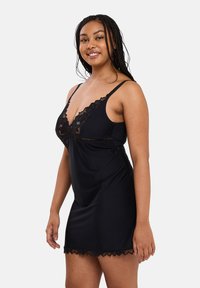 Black satin nightdress with lace trim and V-neckline. Features thin shoulder straps and a flowy design, ending above the knee.