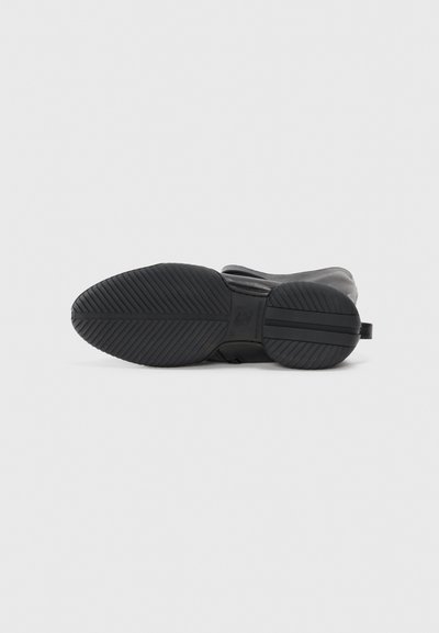 Pantof din material negru sportiv, cu o talpă din cauciuc texturat, având un superior neted și un design minimalist. Talpa dispune de modele distinctive pentru aderență.