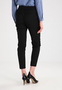Pantaloni neri su misura con vita elastica, vestibilità slim e tasche posteriori. Abbinati a scarpe con tacco alto nere e lucide.
