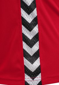 Czerwony strój sportowy z bocznym wzorem w czarno-białe zygzaki na teksturowanej tkaninie. Gładkie wykończenie z widocznym szwem.