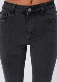Jeans in denim nero con un design aderente, dotati di chiusura frontale con bottone, stile a cinque tasche e superficie liscia.