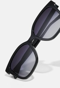 Μαύρα υπερμεγέθη γυαλιά ηλίου με ημιτονικά σκούρα φακό. Διαθέτουν γυαλιστερό σκελετό και φαρδιά, τετράγωνη μορφή, κατάλληλα για διάφορους τύπους προσώπου.