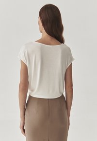 Blouse blanche à manches courtes avec une coupe décontractée, fabriquée en tissu léger, qui tombe doucement sur les épaules, associée à une jupe crayon marron.