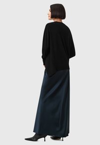 Svart strikket oversized genser kombinert med et lang, mørkt teal skirt i satin og svarte spissede hæler. Glatte teksturer og avslappet silhuett.
