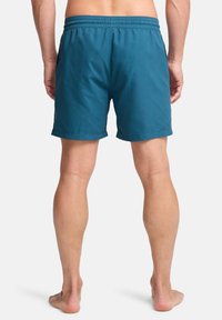Bañador en color teal con cintura elástica, dos bolsillos laterales y un corte relajado. La tela tiene una textura suave y es ligera.