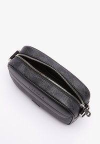 Borsa a tracolla nera con texture Lacoste, con zip argentata parzialmente aperta e fibbia per cinture regolabile su sfondo bianco.