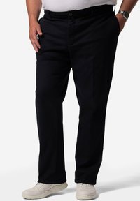 Mörkblå bomullsbukser med rak bendesign, med en framknäppning och sidofickor, som bärs med ljusa sneakers.