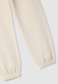 Pantaloni della tuta color beige chiaro con polsini elasticizzati, realizzati in tessuto morbido. Presentano una texture liscia e un design a vestibilità rilassata.