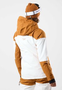 Giacca da sci marrone e bianca con cappuccio e cerniere sulle maniche. Presenta una texture liscia e un marchio ricamato. Abbinata a pantaloni coordinati.