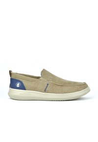 Zapatos deslizables fabricados con un tejido beis de textura suave. Presentan un acento azul en el talón y una suela de goma para mayor agarre. Detalles de costura mínimos.