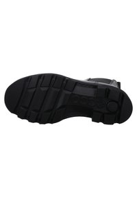 Semelle de chaussure en caoutchouc noir avec de profonds rainures pour une traction, présentant un motif texturé et un logo en relief pour une meilleure adhérence et stabilité.