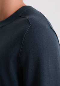 Pull en maille bleu marine présentant une texture lisse, un col rond et des manches montées avec des détails de couture subtils.