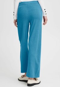 Blauwe wijde broek van zacht, rekbaar materiaal met een gladde textuur en een elastische tailleband. Gecombineerd met crèmekleurige schoenen met gouden accenten.