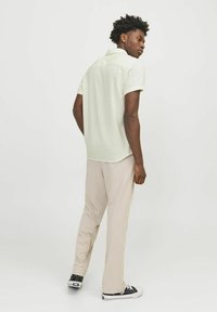 Chemise à manches courtes, vert clair, à boutons, avec une finition texturée, associée à un pantalon crème et des baskets noires. Design simple.