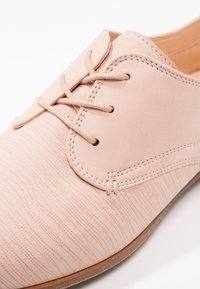 Chaussure en cuir rose avec une texture subtile, dotée d'un bout arrondi et de lacets classiques. Les détails de couture ajoutent structure et raffinement.