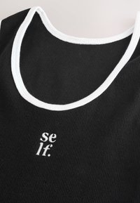 Juodas raukšlėtas marškinėlių viršus su baltu apvadu. Yra mažas baltas logotipas, skaitantis "se lf." Sukurtas su klasikinėmis apvaliais iškirpimu.