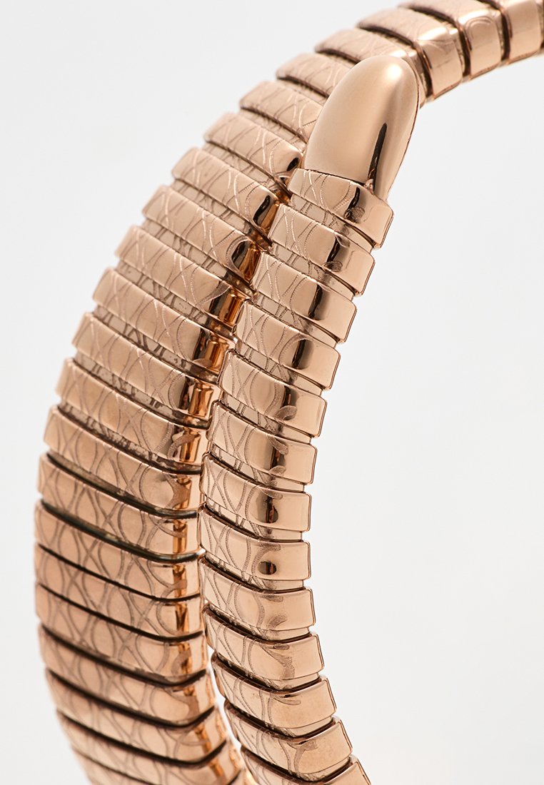 Pulsera elástica de oro rosa con un diseño texturizado, que presenta segmentos alargados e interconectados y un detalle de cierre liso y redondeado.