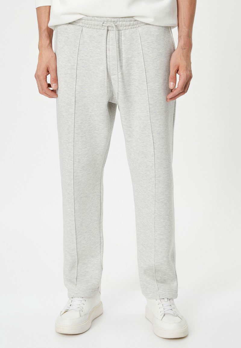 Pantalones de chándal gris claro con cinturilla elástica, costuras frontales planas y un ajuste relajado. Combinados con zapatillas blancas.