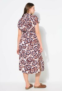 Vestido fluido de flores con mangas cortas, que presenta un fondo rosa, un patrón de flores grandes en azul y marrón, y un detalle de cintura atada.