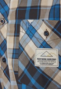 Braunes, beiges und blaues kariertes Hemd mit Knopfverschluss; verfügt über eine linke Brusttasche mit gestickten Initialen und einem Markenetikett-Patch.