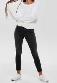 Pull blanc en maille, jean skinny noir et baskets blanches. Le pull présente une coupe décontractée, tandis que le jean a un design classique.