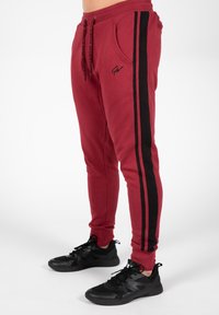 Rode joggerbroeken met zwarte zijstrepen, een elastische tailleband en zakken, gemaakt van een zachte stof. Gecombineerd met zwarte sportschoenen.