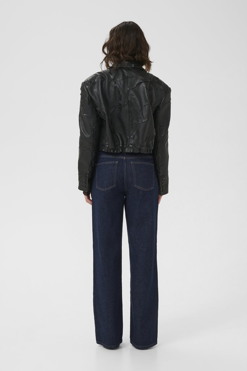 Svart kort läderjacka med en strukturerad finish, med en bred krage och knappade ärmslut, kombinerad med högmidjade mörkblå jeans.
