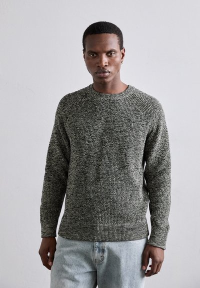 Pull en tricot gris texturé avec un col rond, des manches longues et une coupe légèrement décontractée. Porté avec un jean en denim bleu clair.